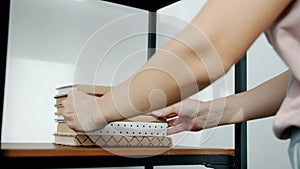 Close-up of female hands putting pile of books onto wooden shelf