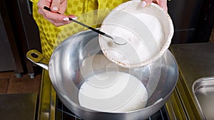 Close-up of female hands putting sugar in hot milk while preparing dough for muffins in the kitchen.