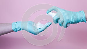 Close-up of female hands with rubber glove pumping cleansing foam on pink background. Concept of face cleanser, cosmetics