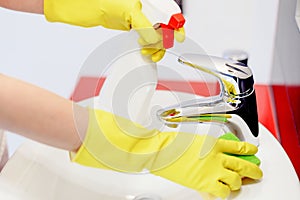 Close up of female hands with rubber gloves cleaning tap.