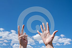 Close-up of female hands showing seven fingers on a blue sky background. Number seven in sign language. Copy space
