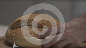 Close up of female hands slicing white bread in slow motion on a wooden board. Action. Cutting freshly baked round