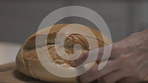 Close up of female hands slicing white bread in slow motion on a wooden board. Action. Cutting freshly baked round
