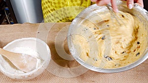 Close-up of female hands stirring the dough with a whisk while preparing delicious Easter cakes or muffins with raisins