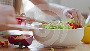 Close-up female hands stirring with wooden spoon ingredients vegetables in fresh delicious salad, unrecognizable family