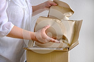 Close-up of female hands take out package from open cardboard box of medium size postal box with wrapping paper, a parcel,