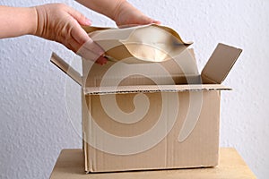 Close-up of female hands take out package from open cardboard box of medium size postal box with wrapping paper, a parcel,