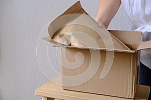 Close-up of female hands take out package from open cardboard box of medium size postal box with wrapping paper, a parcel,