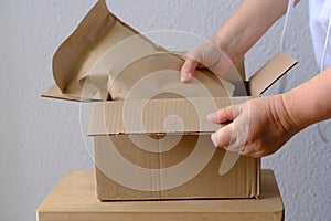 close-up of female hands take out package from open cardboard box of medium size postal box with wrapping paper, a parcel,