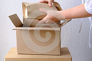 Close-up of female hands take out package from open cardboard box of medium size postal box with wrapping paper, parcel, delivery