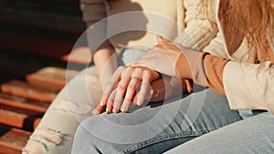 Close up of female hands of two friends girls sitting outdoors. Caring young woman holding hand supporting her friend
