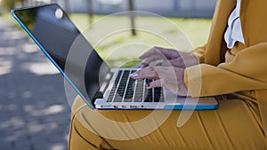 Close-up of a female hands typing on computer keyboard. Outdoors. Young business woman in suit sitting on the bench and