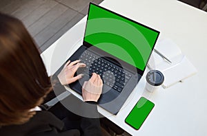 Close-up of female hands typing on laptop keyboard with a green chromakey screen for ads. Mobile phone with green screen and copy