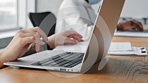 Close-up female hands typing on laptop keyboard, holding document paper checking data in report and entering information