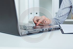 Close up of female hands typing on laptop keyboard in office background.