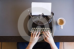 Close up of female hands typing on retro typewriter. Cup of coffee is at right side.Indoors. Top view.