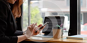 Close up of female hands using modern smart phone while working at office with computer, businesswoman typing text