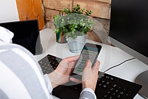 Close-up of female hands using modern smart phone while working at office with computer, businesswoman typing text message on her