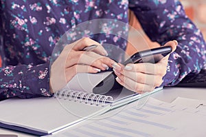 Close-up of female hands using smart phone while working on computer at modern office interior, businesswoman typing