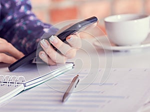 Close-up of female hands using smart phone while working on computer at modern office interior, businesswoman typing