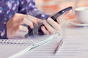 Close-up of female hands using smart phone while working on computer at modern office interior, businesswoman typing