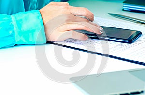 Close-up of female hands using smart phone while working on computer at modern office interior, businesswoman typing