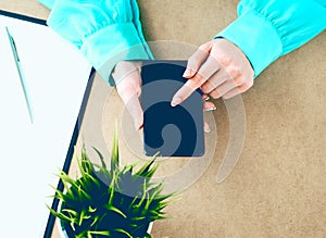 Close-up of female hands using smart phone while working on computer at modern office interior, businesswoman typing