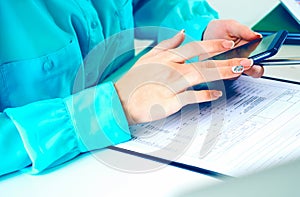 Close-up of female hands using smart phone while working on computer at modern office interior, businesswoman typing