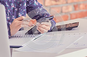 Close-up of female hands using smart phone while working on computer at modern office interior, businesswoman typing