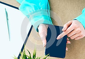 Close-up of female hands using smart phone while working on computer at modern office interior, businesswoman typing