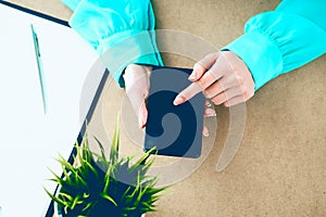 Close-up of female hands using smart phone while working on computer at modern office interior, businesswoman typing