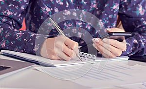 Close-up of female hands using smart phone while working on computer at modern office interior, businesswoman typing