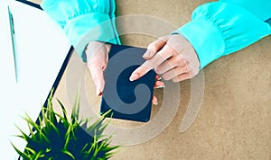 Close-up of female hands using smart phone while working on computer at modern office interior, businesswoman typing