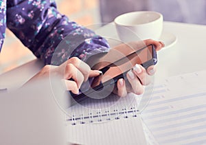 Close-up of female hands using smart phone while working on computer at modern office interior, businesswoman typing