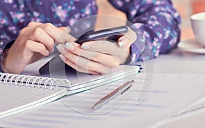 Close-up of female hands using smart phone while working on computer at modern office interior, businesswoman typing