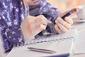 Close-up of female hands using smart phone while working on computer at modern office interior, businesswoman typing