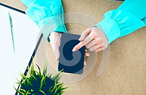 Close-up of female hands using smart phone while working on computer at modern office interior, businesswoman typing