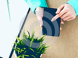 Close-up of female hands using smart phone while working on computer at modern office interior, businesswoman typing