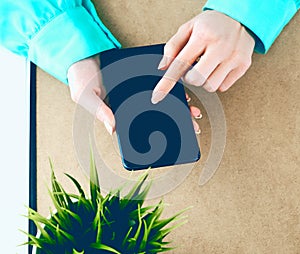 Close-up of female hands using smart phone while working on computer at modern office interior, businesswoman typing