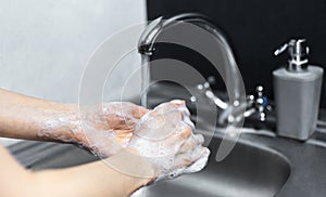 Close-up of female hands washing with soap under the water tap beside grey dispenser bottle with gel. Hygiene concept.