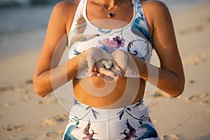 Close up of female hands. Woman holding small white stone in her hands. Heart shape stone. Slim body. Spend time on the beach.