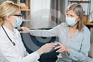 Close-up of female healthcare worker, doctor or nurse, using finger pulse oximeter, while visiting sick patient elderly