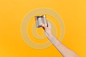 Close up female hold in hand clear empty blank iron metal chrome can canned goods food isolated on yellow background