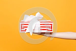 Close up female hold in hand red white striped present gift box with ribbon bow isolated on trending yellow orange