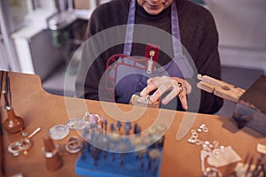 Close Up Of Female Jeweller Working On Piece With Saw In Studio