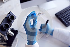 Close Up Of Female Lab Worker Wearing PPE Researching BA.2 Variant Of Covid-19 With Microscope