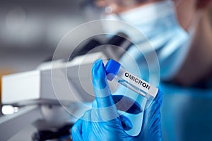 Close Up Of Female Lab Worker Wearing PPE Researching Omicron Variant Of Covid-19 With Microscope