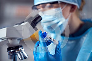 Close Up Of Female Lab Worker Wearing PPE Researching Vaccine With Microscope