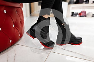 Close up of female legs in fashionable leather black boots with red soles. Girl in stylish jeans in fashion shoes sits on a red