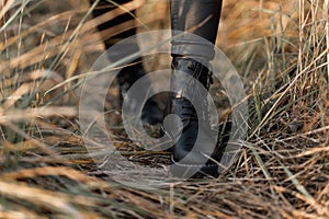 Close up of female legs in fashionable leather black boots. Trendy girl in stylish leggings in fashion shoes walks on the dry